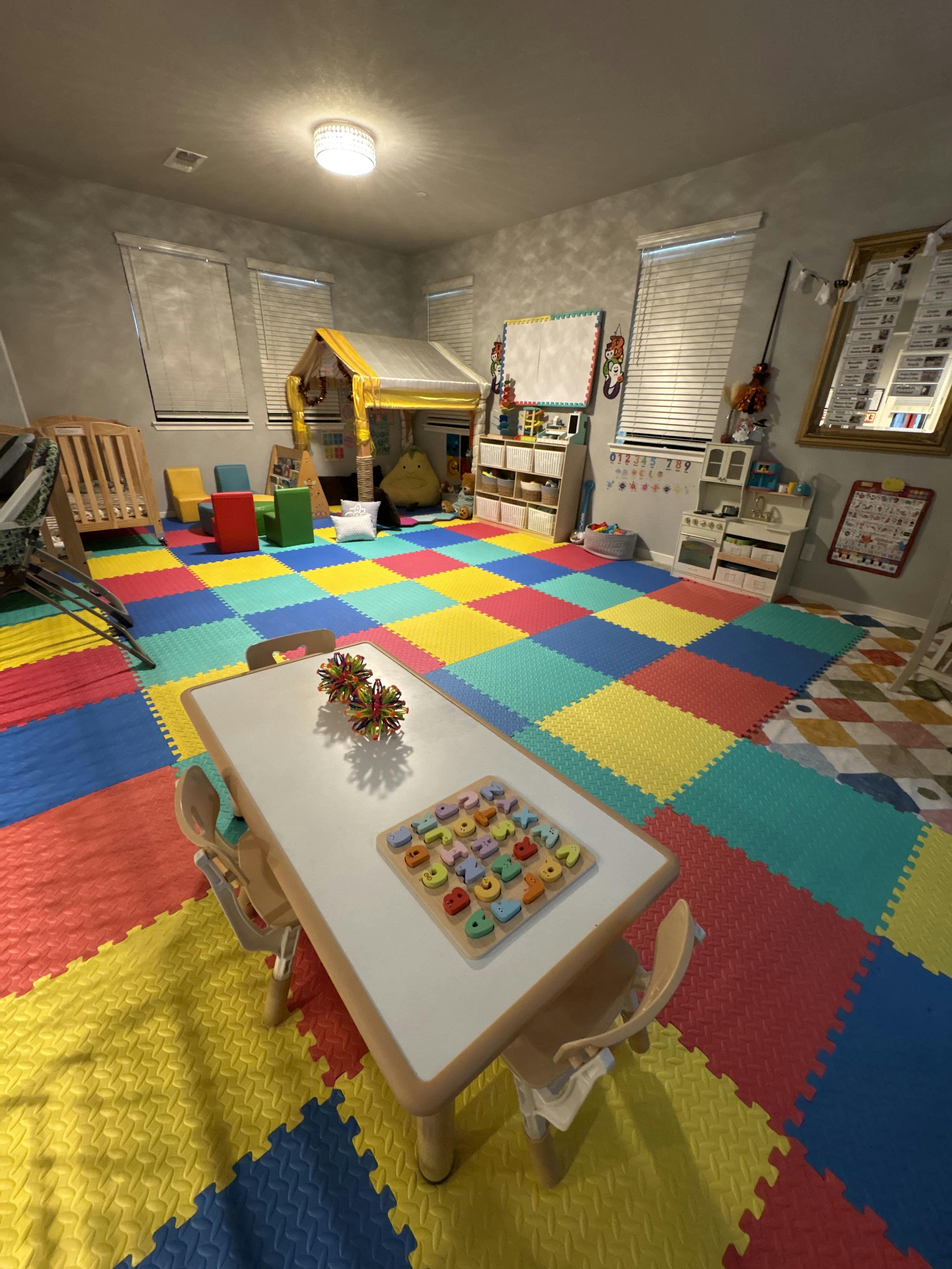 Playroom with a small table and alphabet puzzle, play tent, and floor mats