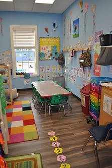 Empty classroom with small tables and chairs, colorful rug and wall decorations