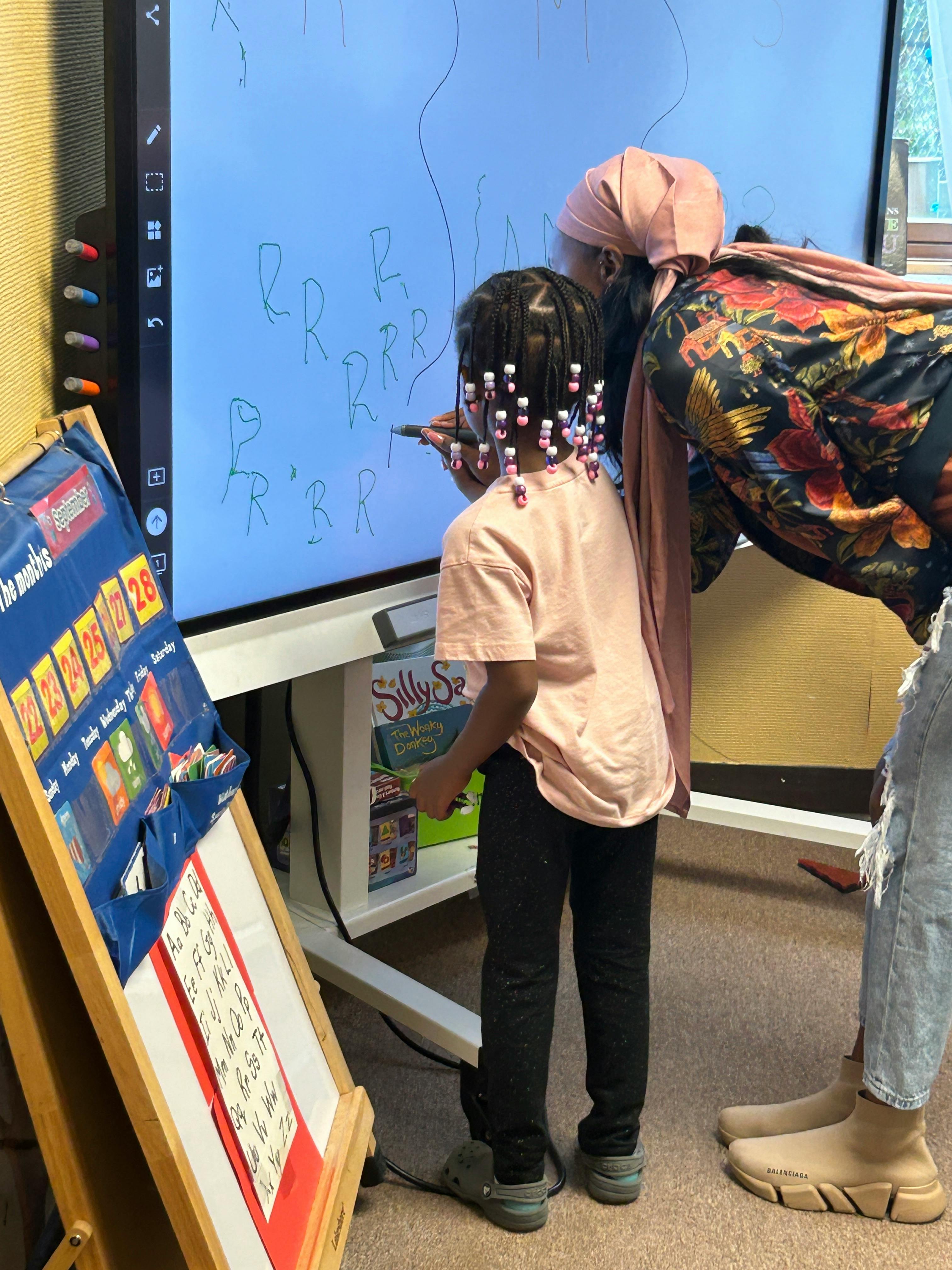 Child and adult writing on an interactive whiteboard