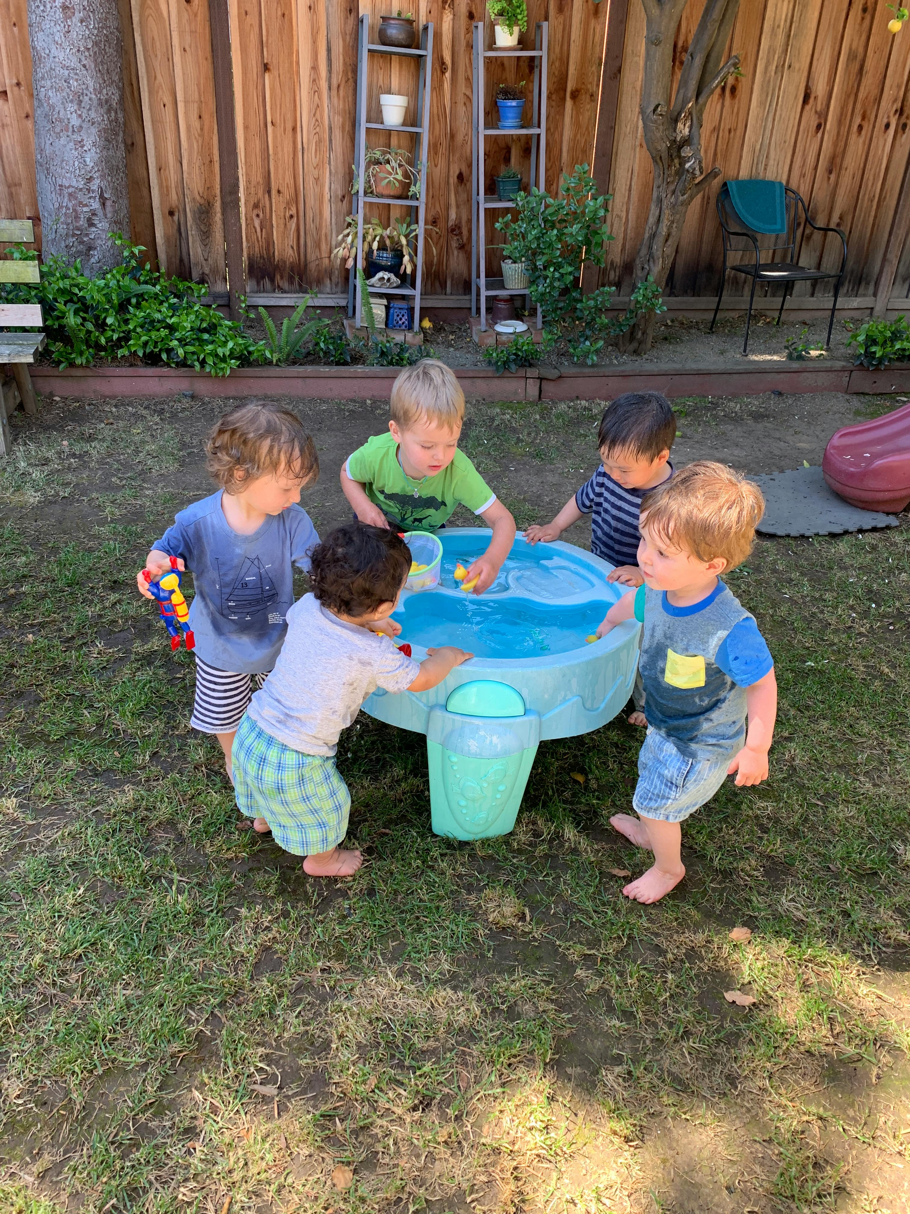 Five children playing around a water table outdoors