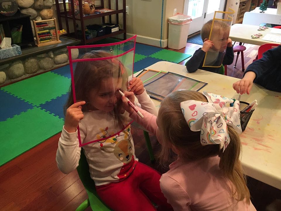 Child holding a clear screen while another child draws on it
