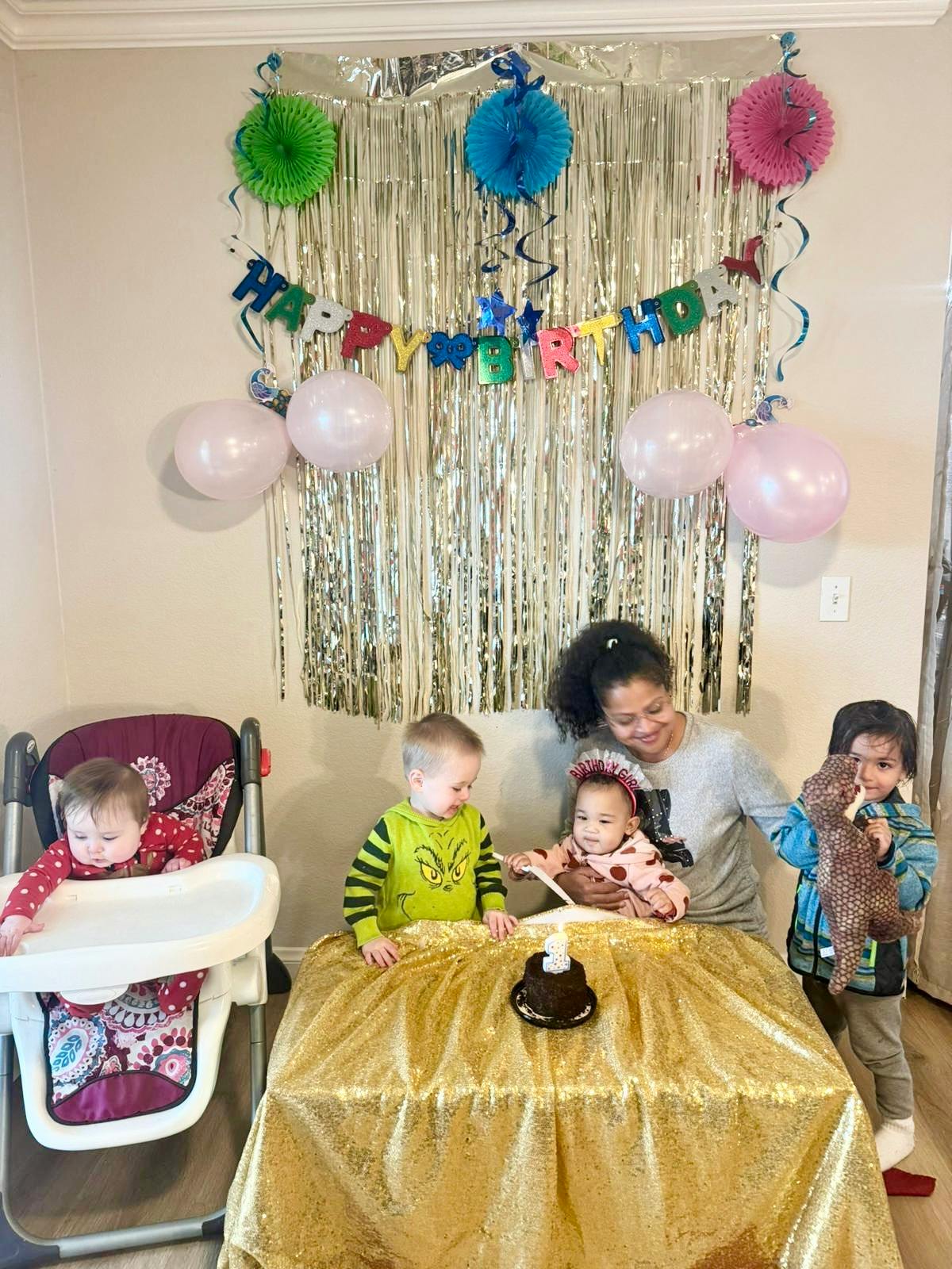 Adult and three children around a table with a small cake, one child in a high chair