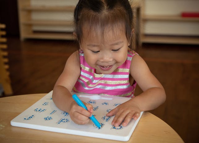 Child drawing on a white board with a blue marker