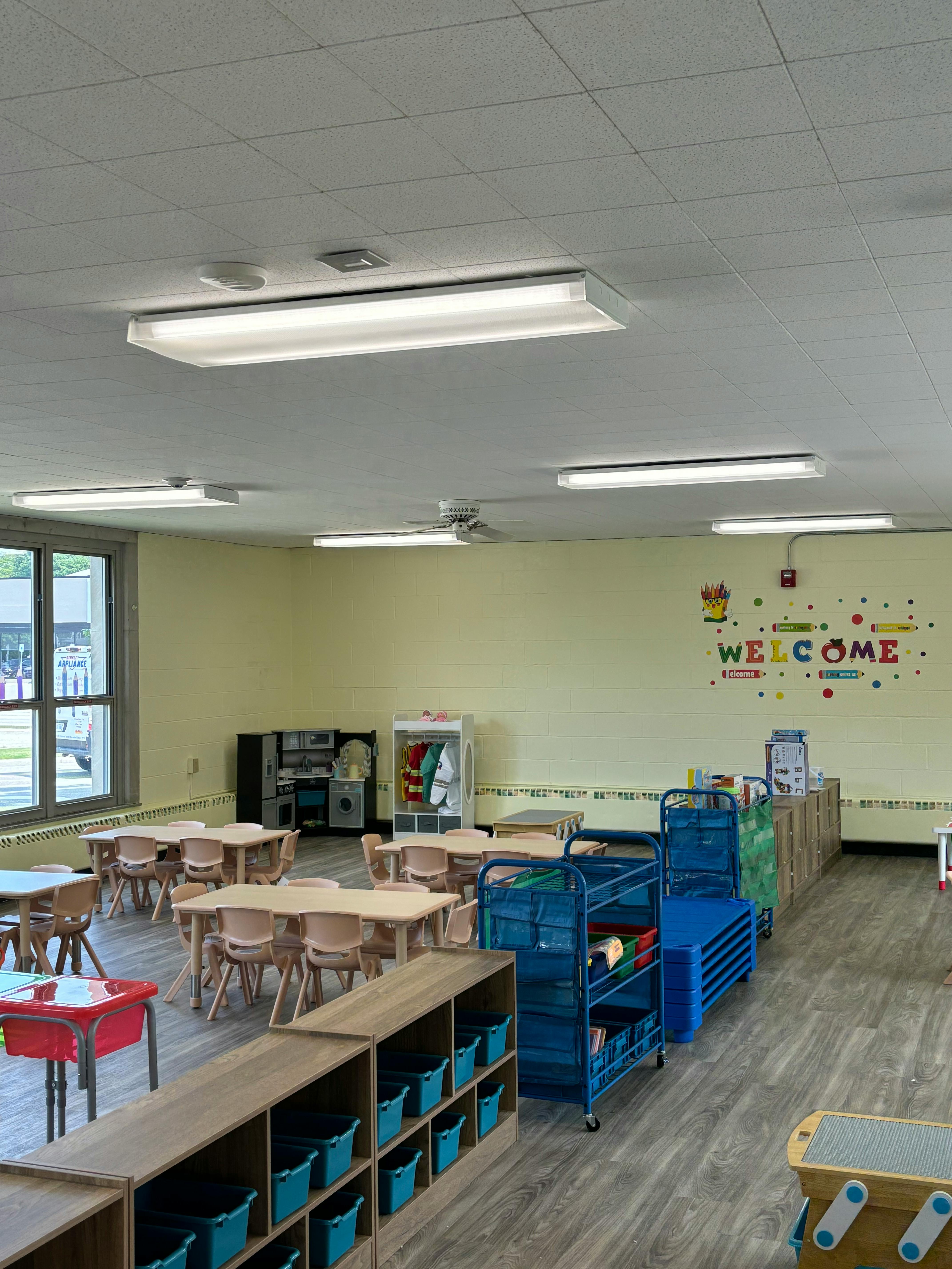 Empty classroom with small tables and chairs, storage units, and a welcome sign