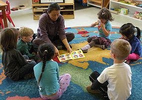 Adult reading book to children sitting on a rug