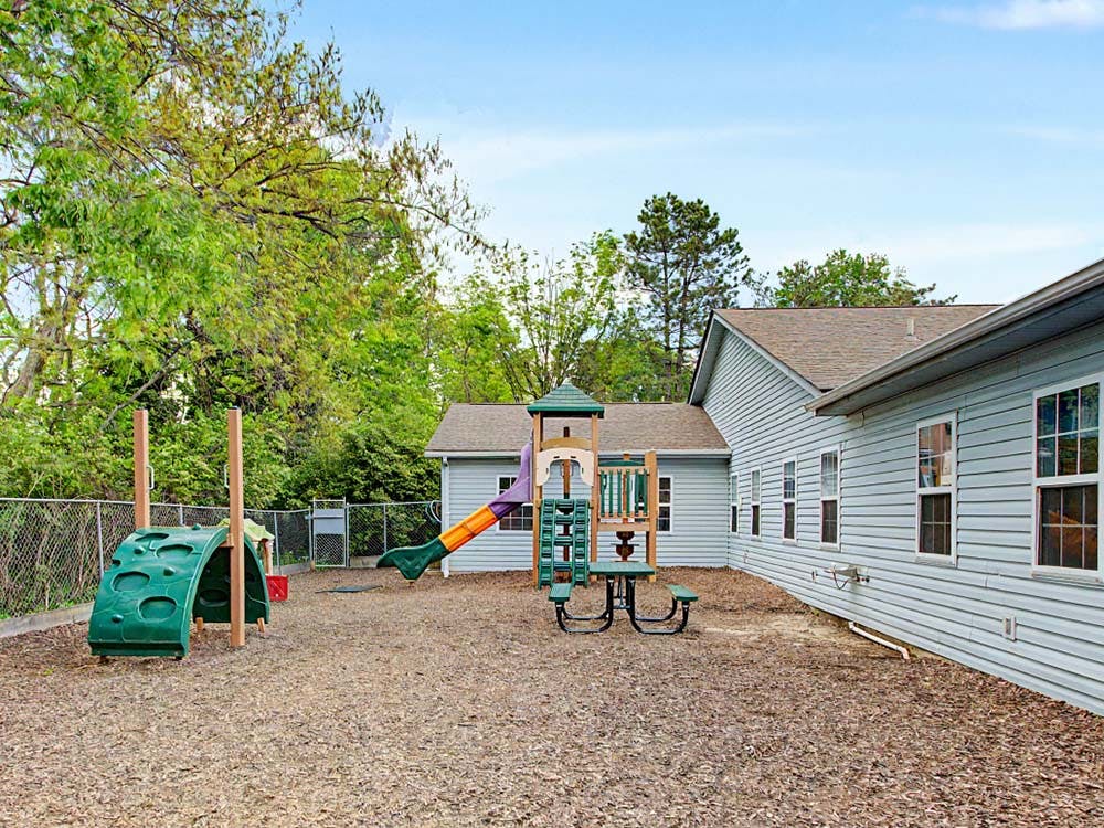 A playground with a climbing structure, slide, and picnic table next to a building