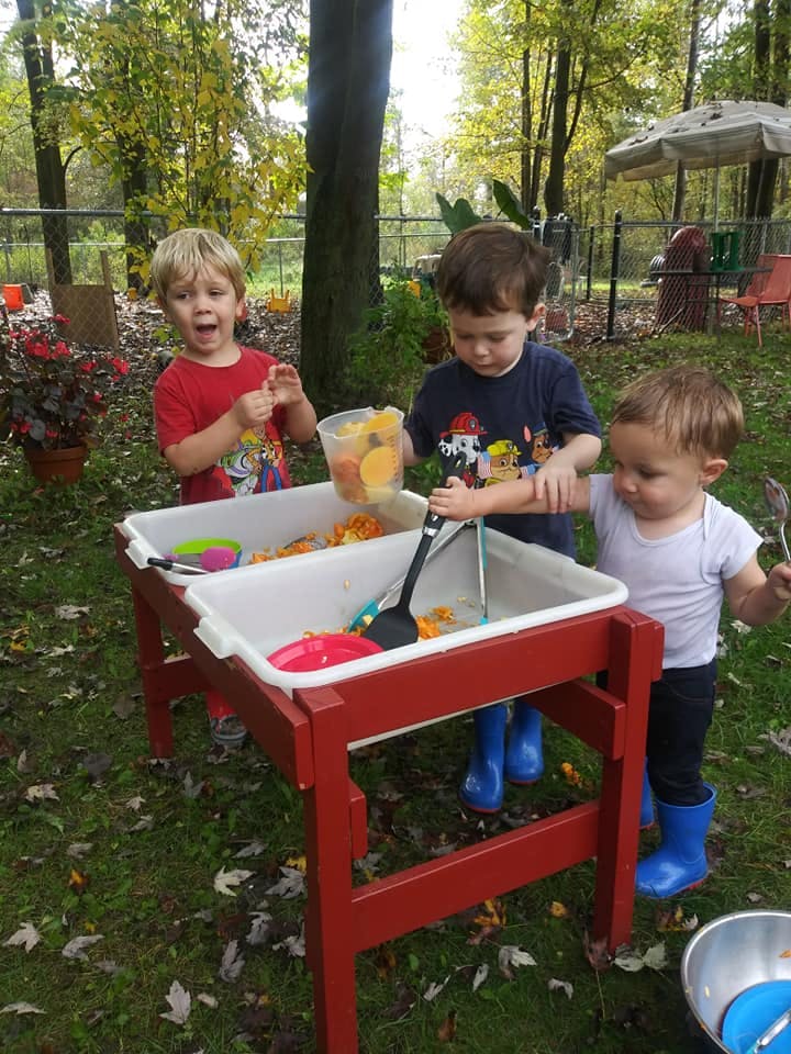 Three children playing with a sensory table outdoors