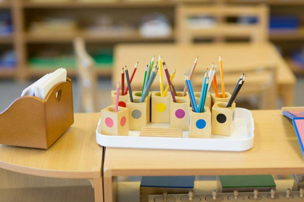 Colored pencils in wooden holders on a table in a classroom