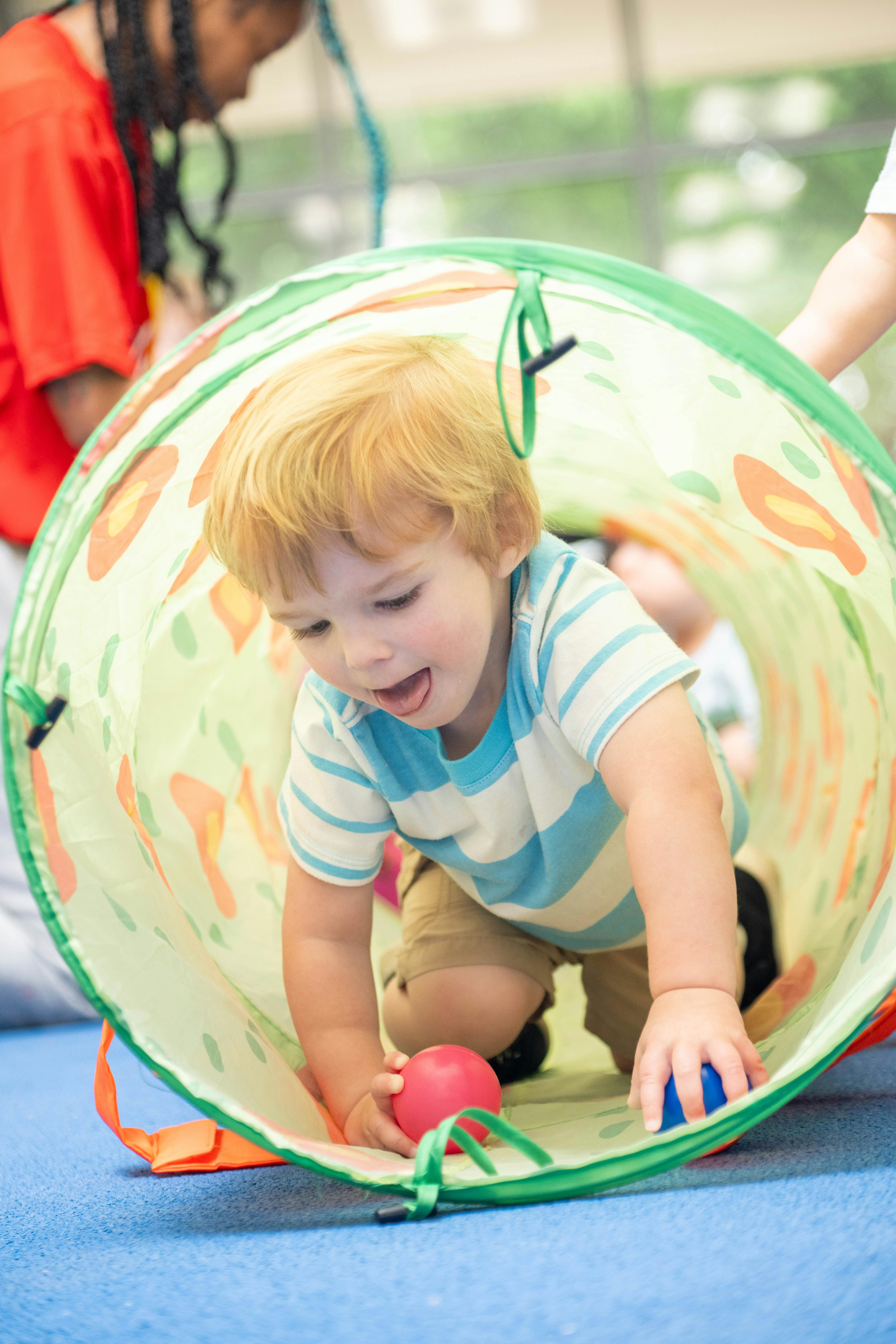 Child crawling through a play tunnel with balls