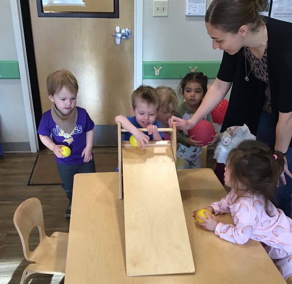 Adult and children playing with balls and a wooden ramp