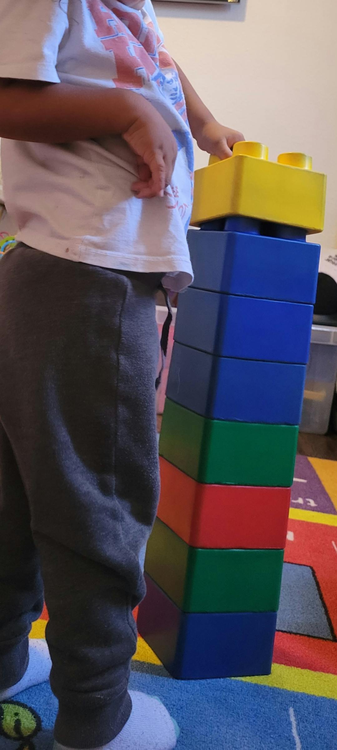 Child standing next to a tall stack of colorful building blocks