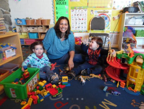 Adult and two children playing with toys on the floor in a classroom