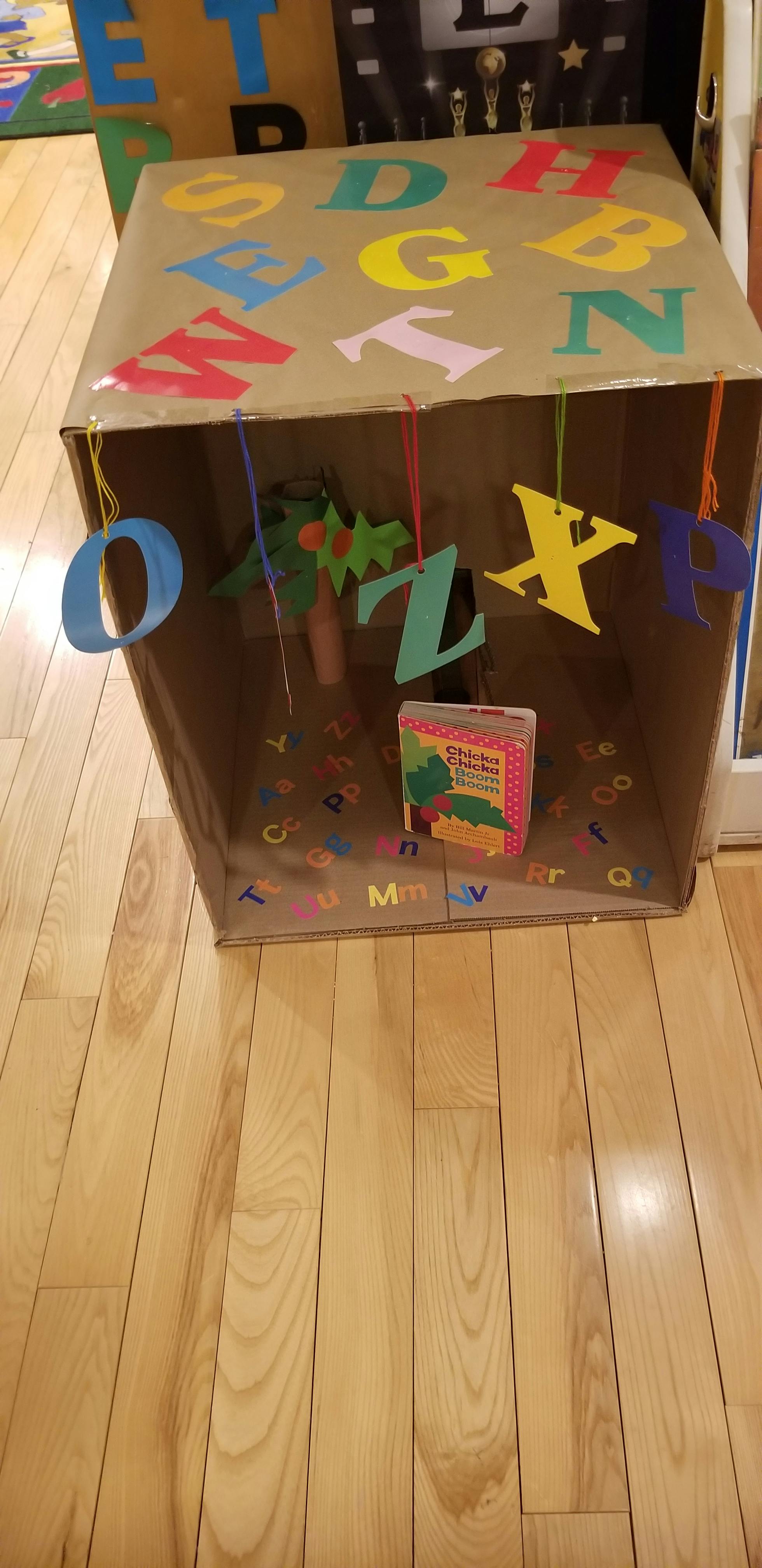 Cardboard box decorated with colorful alphabet letters, a book inside