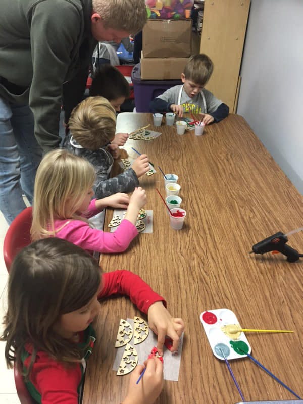 Adult supervising children painting wooden crafts at a table