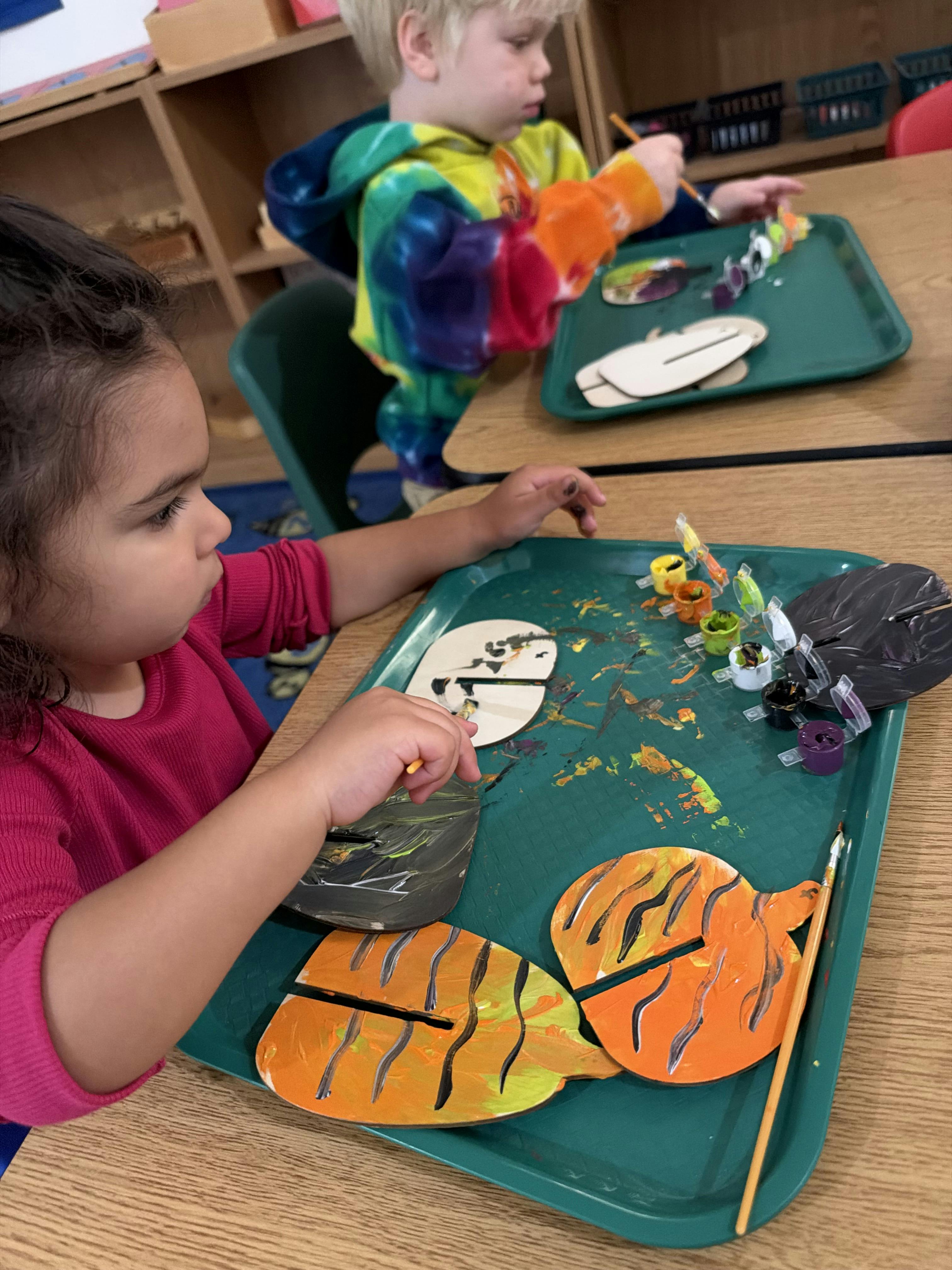 Children painting wooden shapes at a table