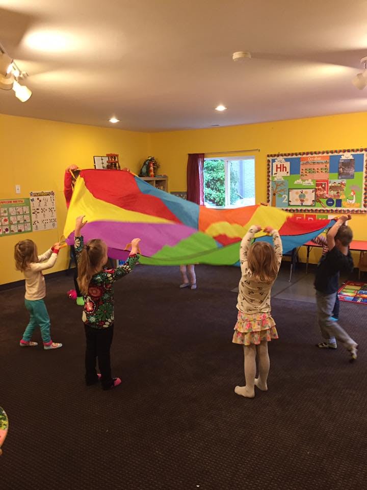 Children playing with a colorful parachute in a classroom