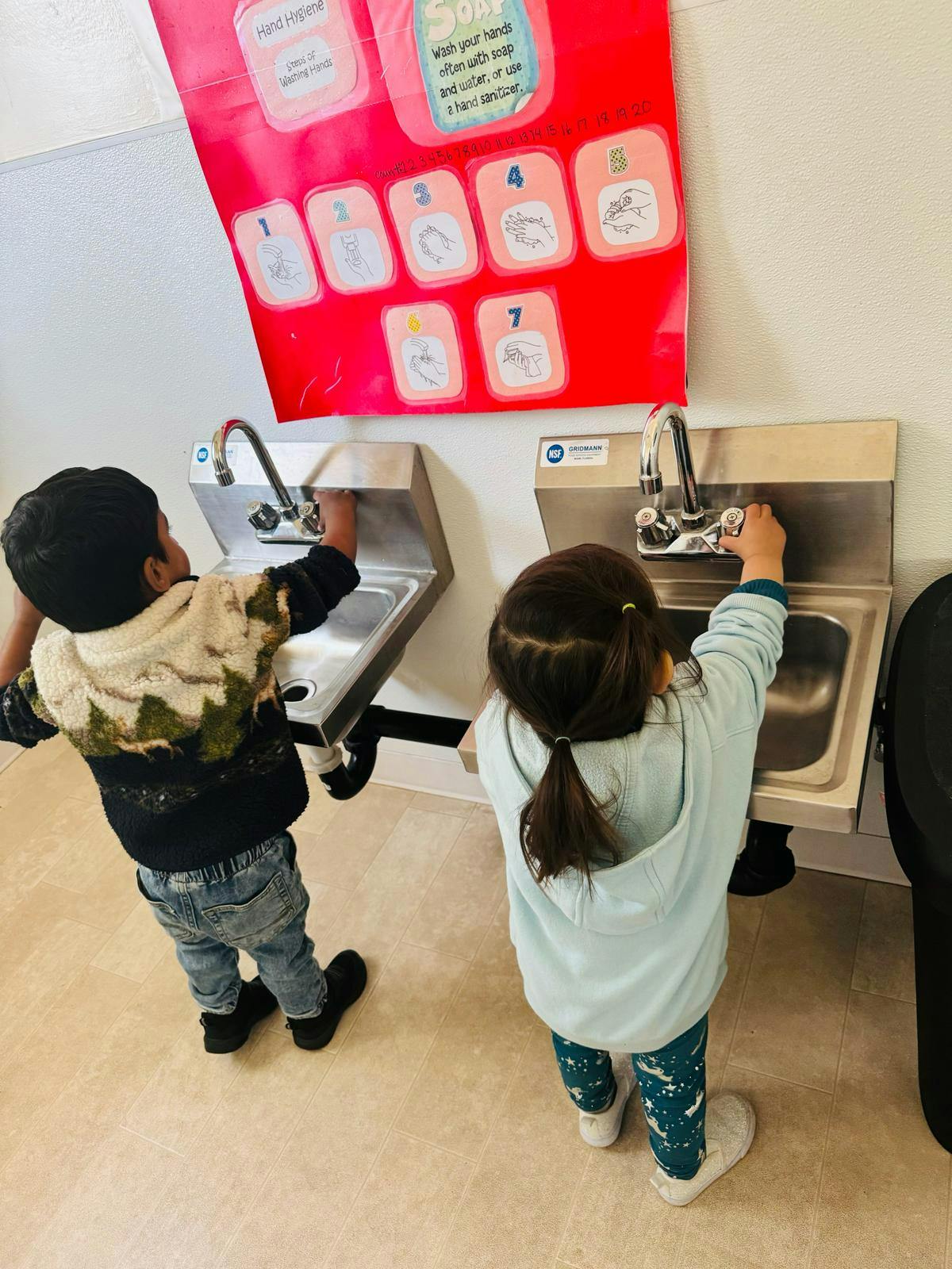 Two children washing hands at sinks in a classroom