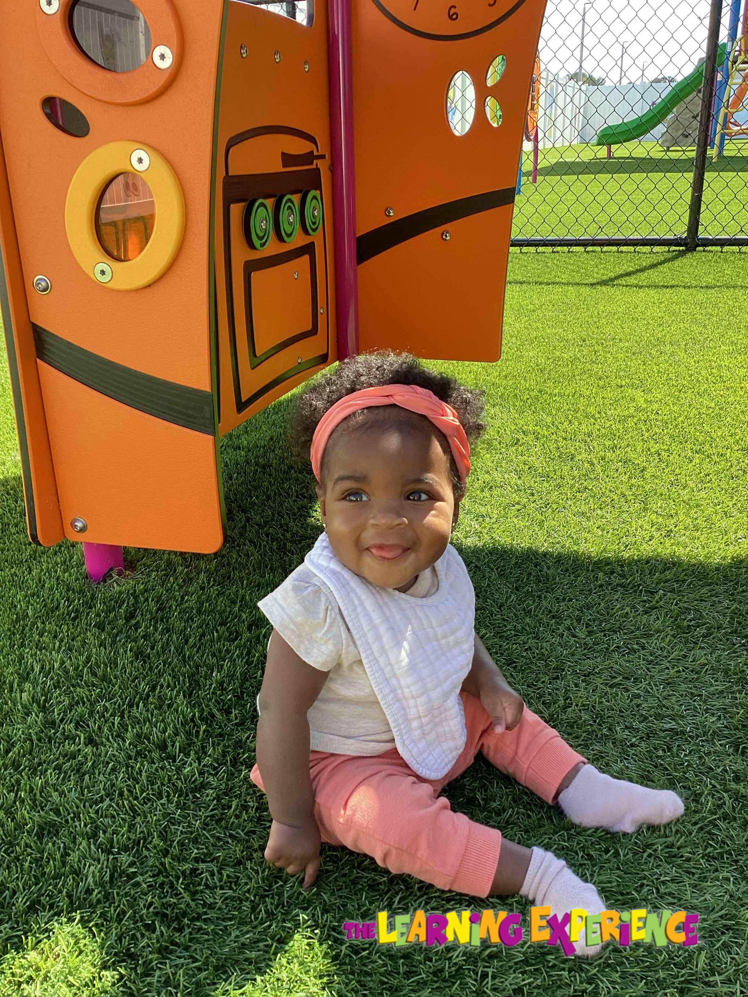Child sitting on artificial grass next to playground equipment