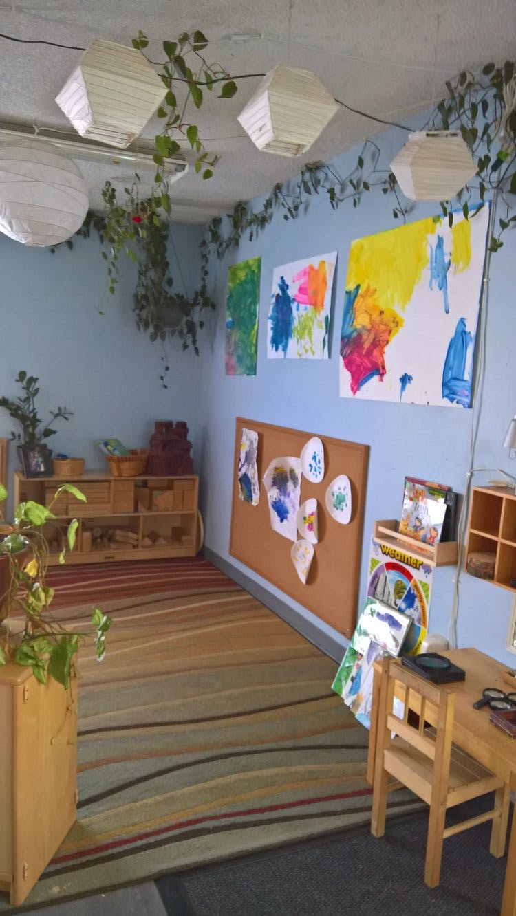 Classroom with children's artwork on walls, cork board, and small wooden furniture