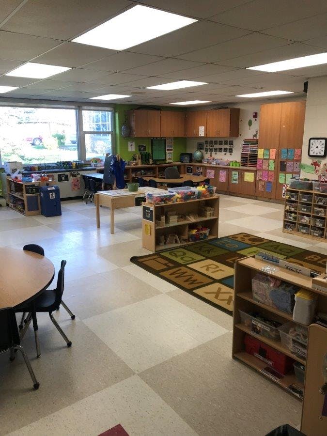 Classroom with tables, chairs, storage shelves, and a rug