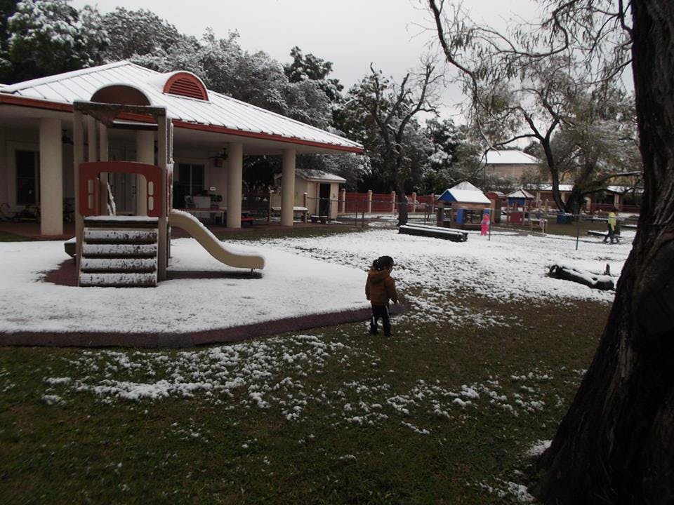 Child standing in a snowy playground with a building and slide