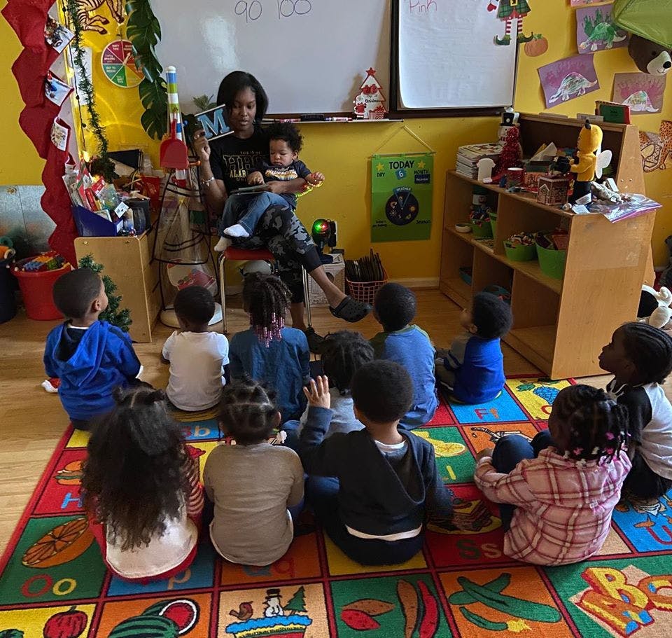 Person holding a child and reading to a group of children in a classroom