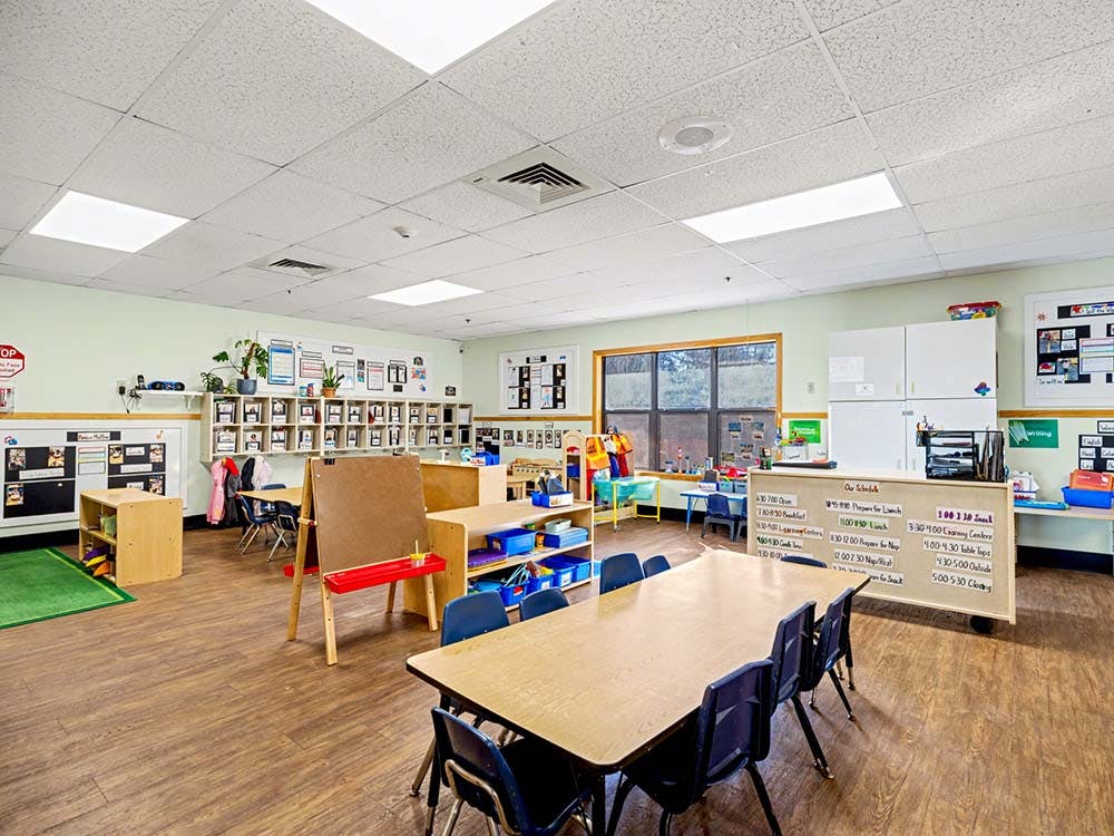 empty preschool classroom with tables, chairs, and learning materials