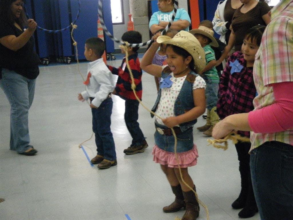 Child in cowboy hat and vest holding a rope with other children
