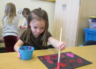 Child painting on black paper with a brush and blue cup