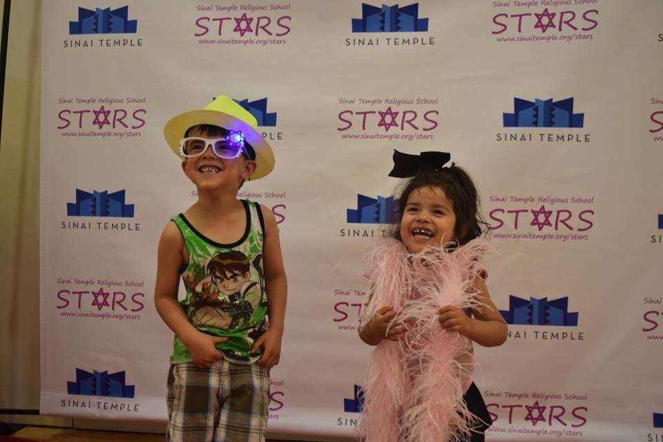 Child in hat and light-up glasses next to child in pink boa