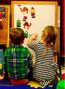 Two children playing with magnets on a whiteboard