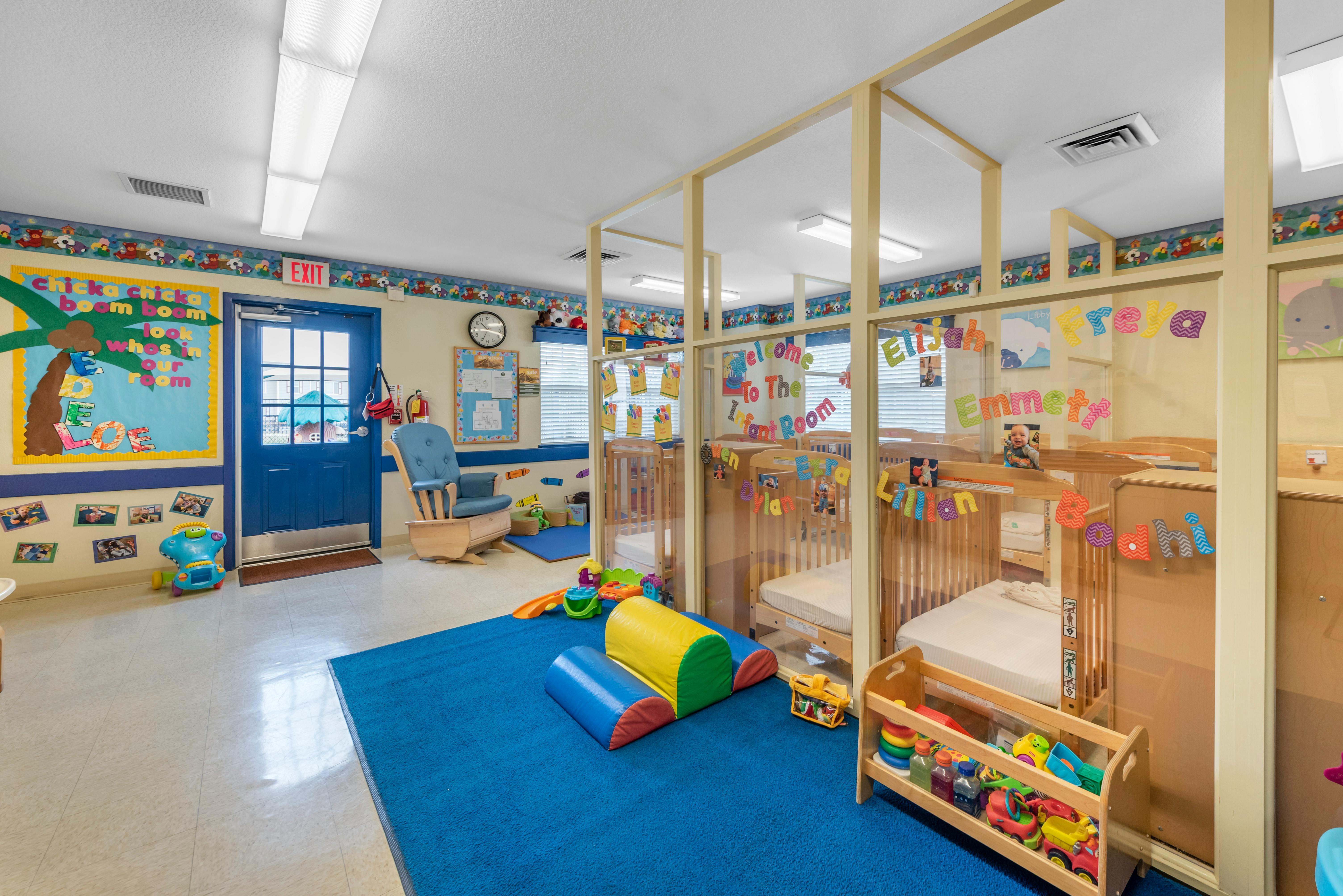 Classroom with cribs, a blue rug, and various children's toys and decorations