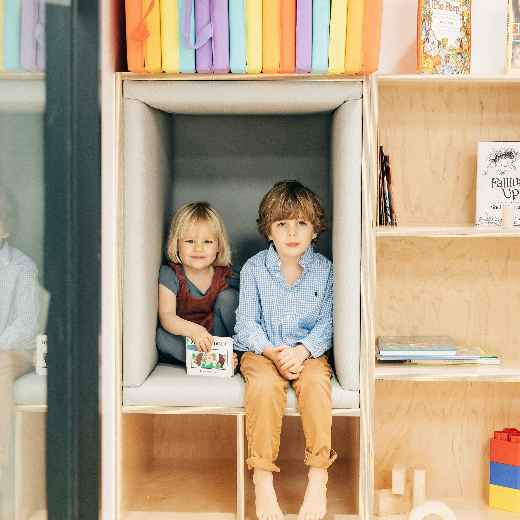Two children sitting in a cubby with a book