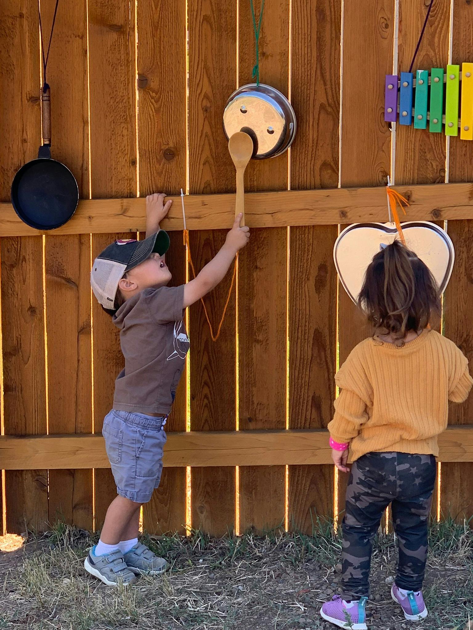 Two children playing with outdoor musical instruments on a wooden fence