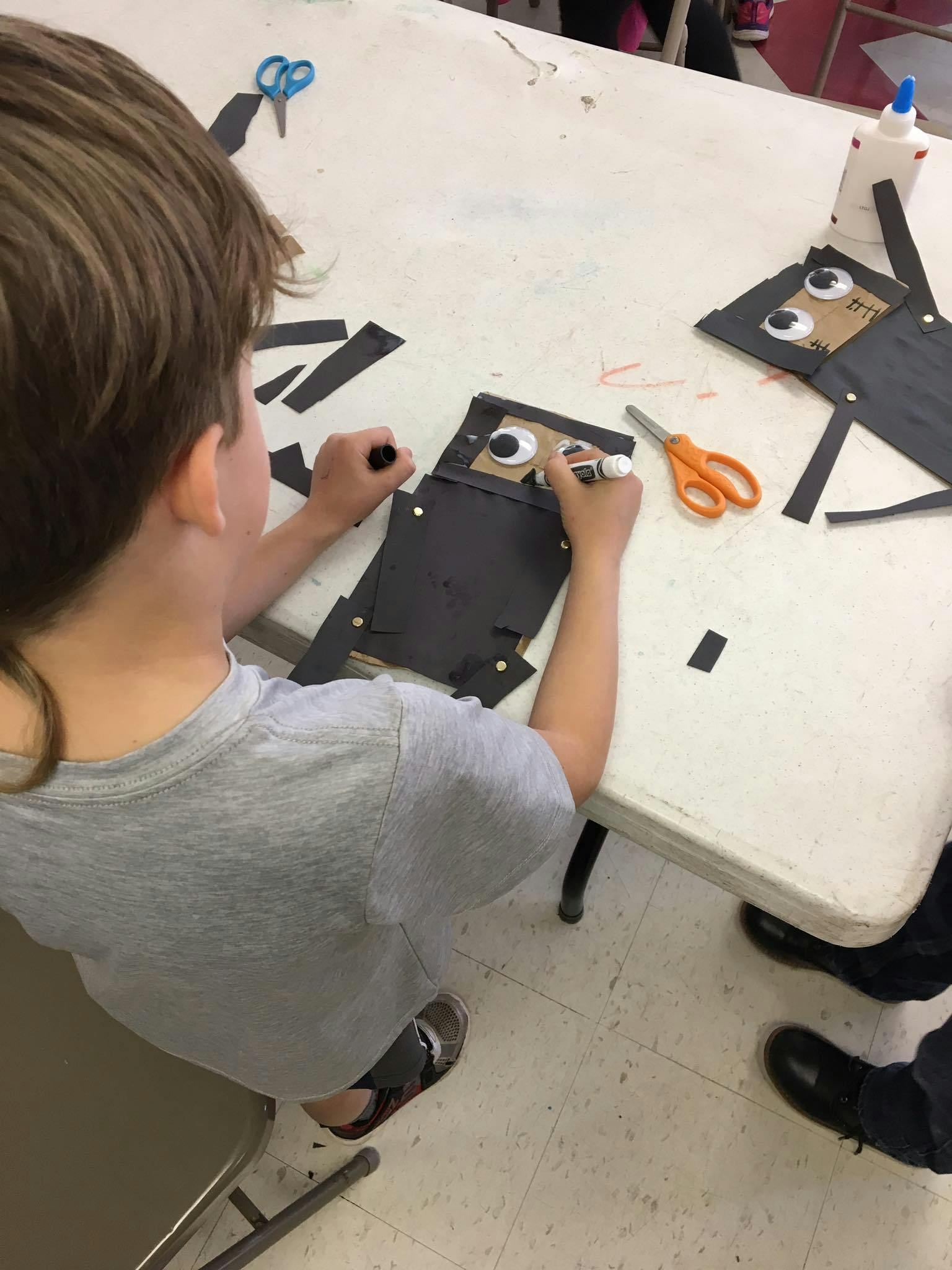 Child making a craft with googly eyes and black paper