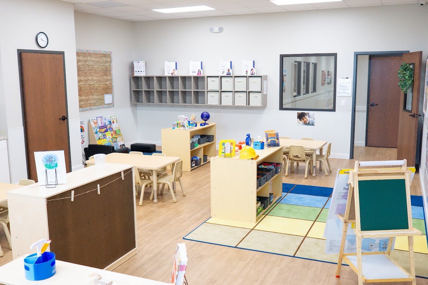 Classroom with small tables, chairs, storage shelves, and an easel