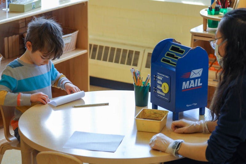 Child and person at a table with a toy mailbox