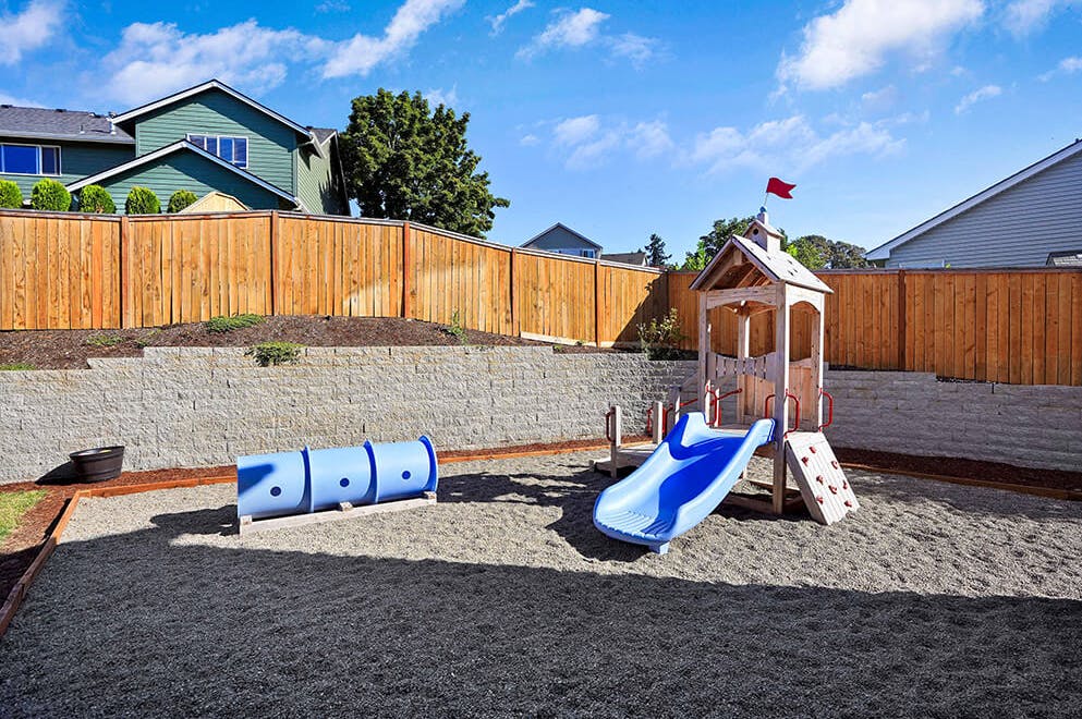Backyard playground with a slide, playhouse, and blue crawl tunnel on gravel