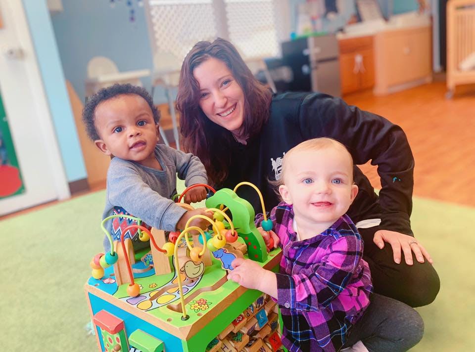 Person kneeling with two children playing with a toy
