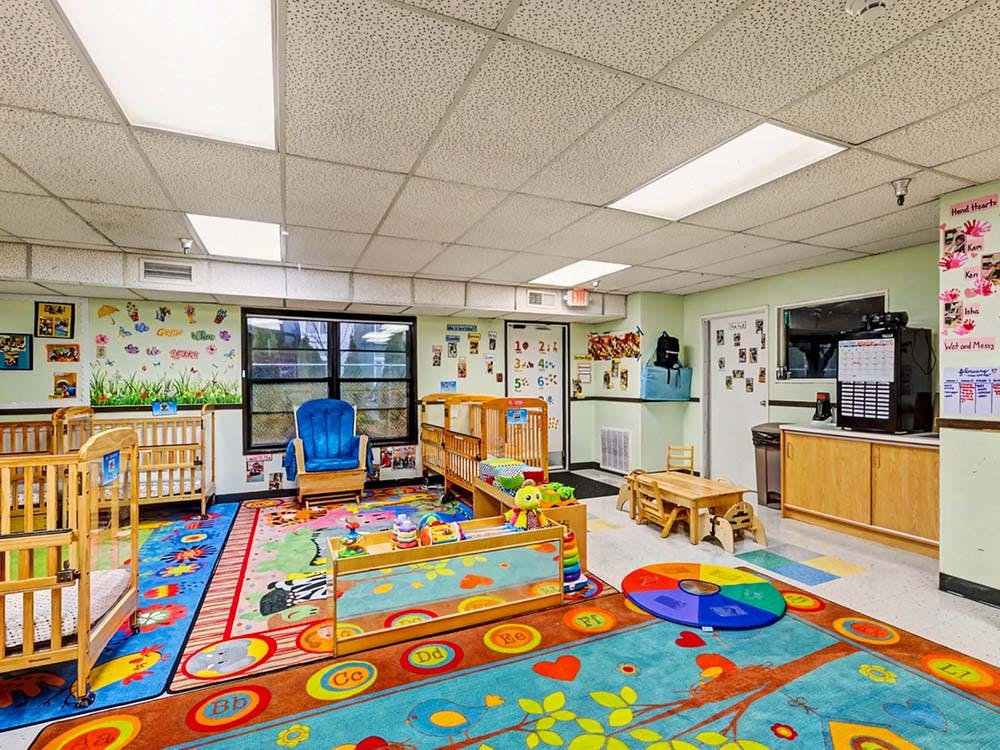 daycare classroom with multiple cribs, colorful rugs, and play furniture
