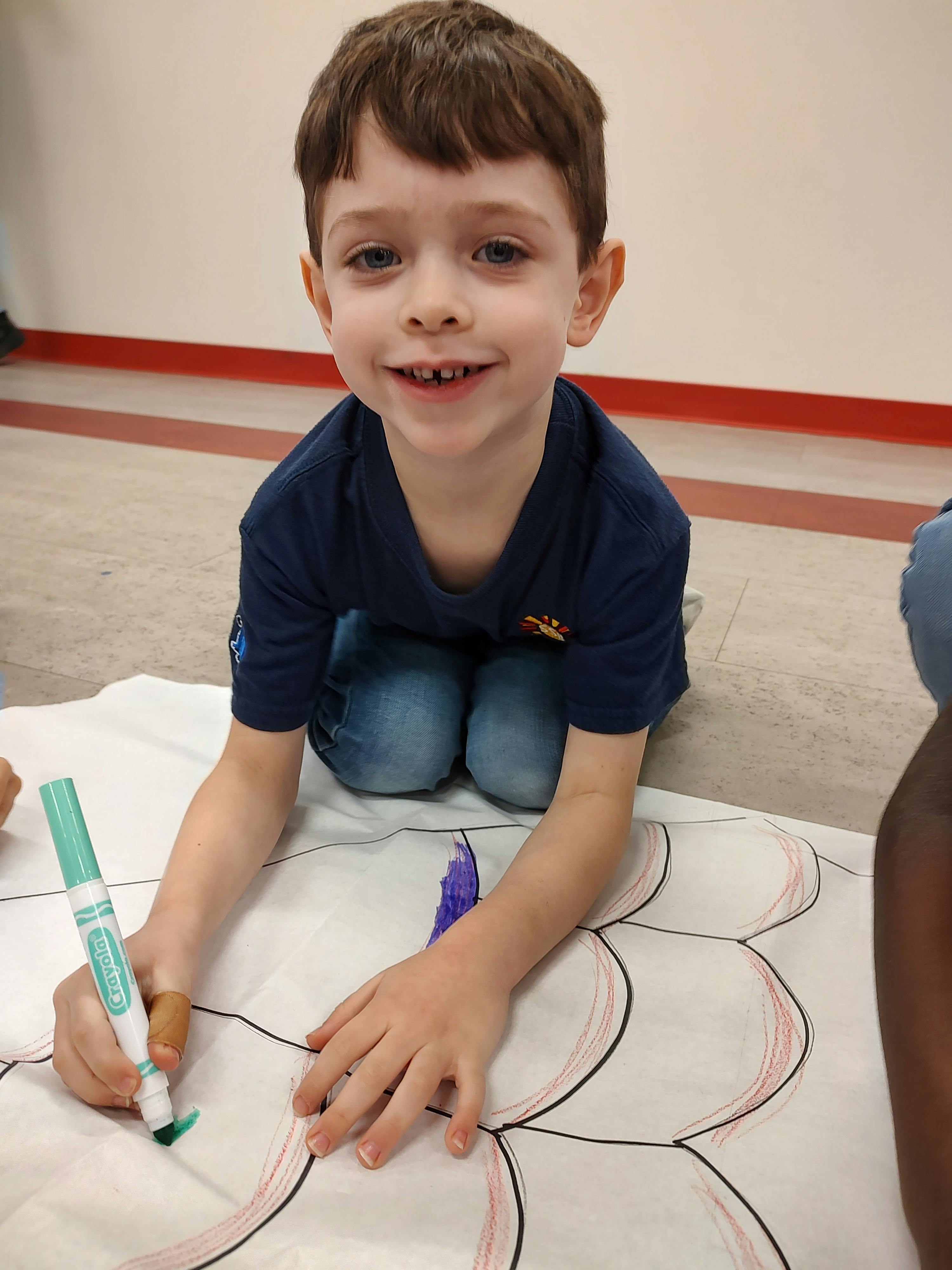 Child kneeling and drawing on paper with a green marker