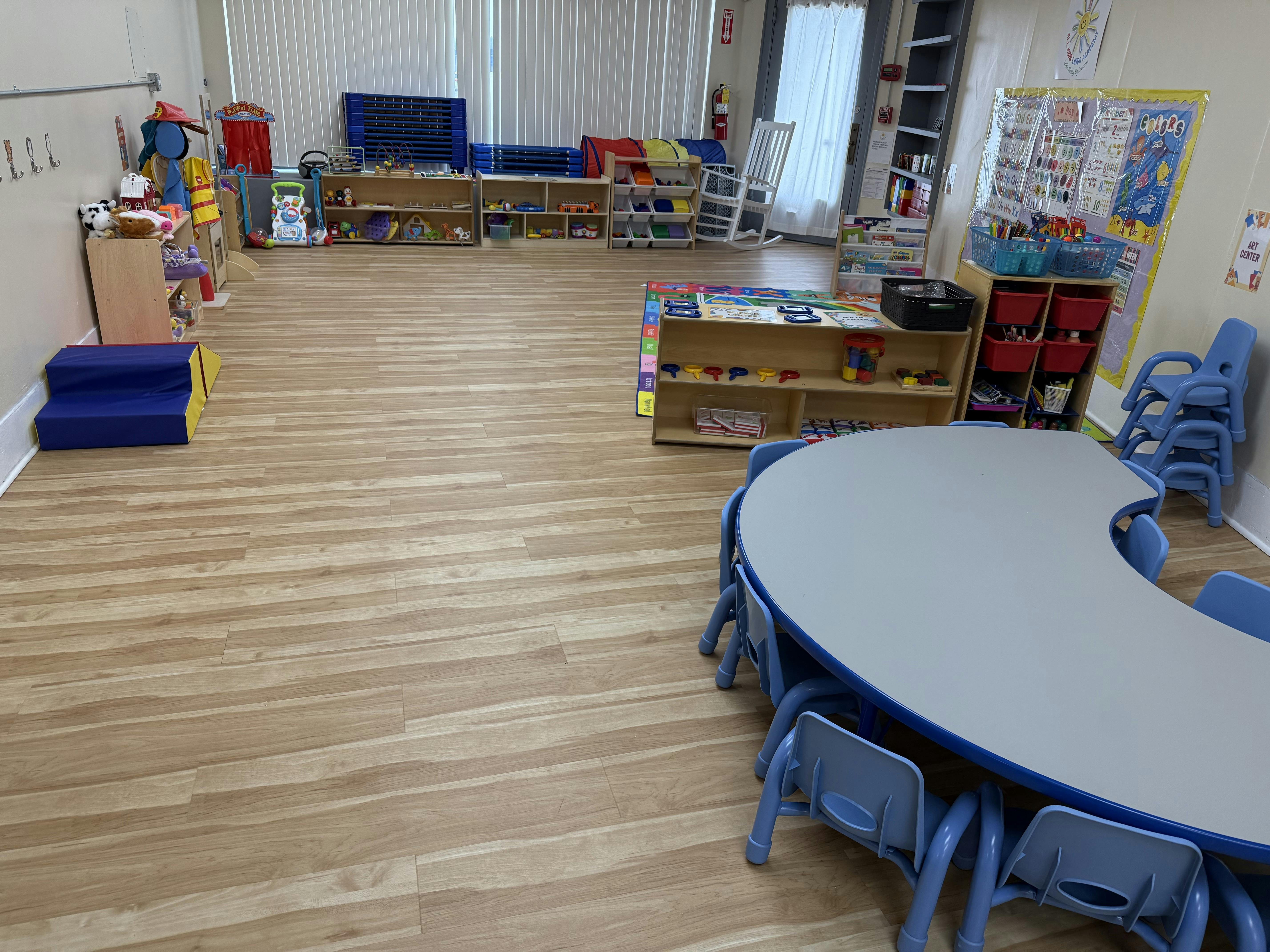 Empty classroom with small tables and chairs, shelves with toys