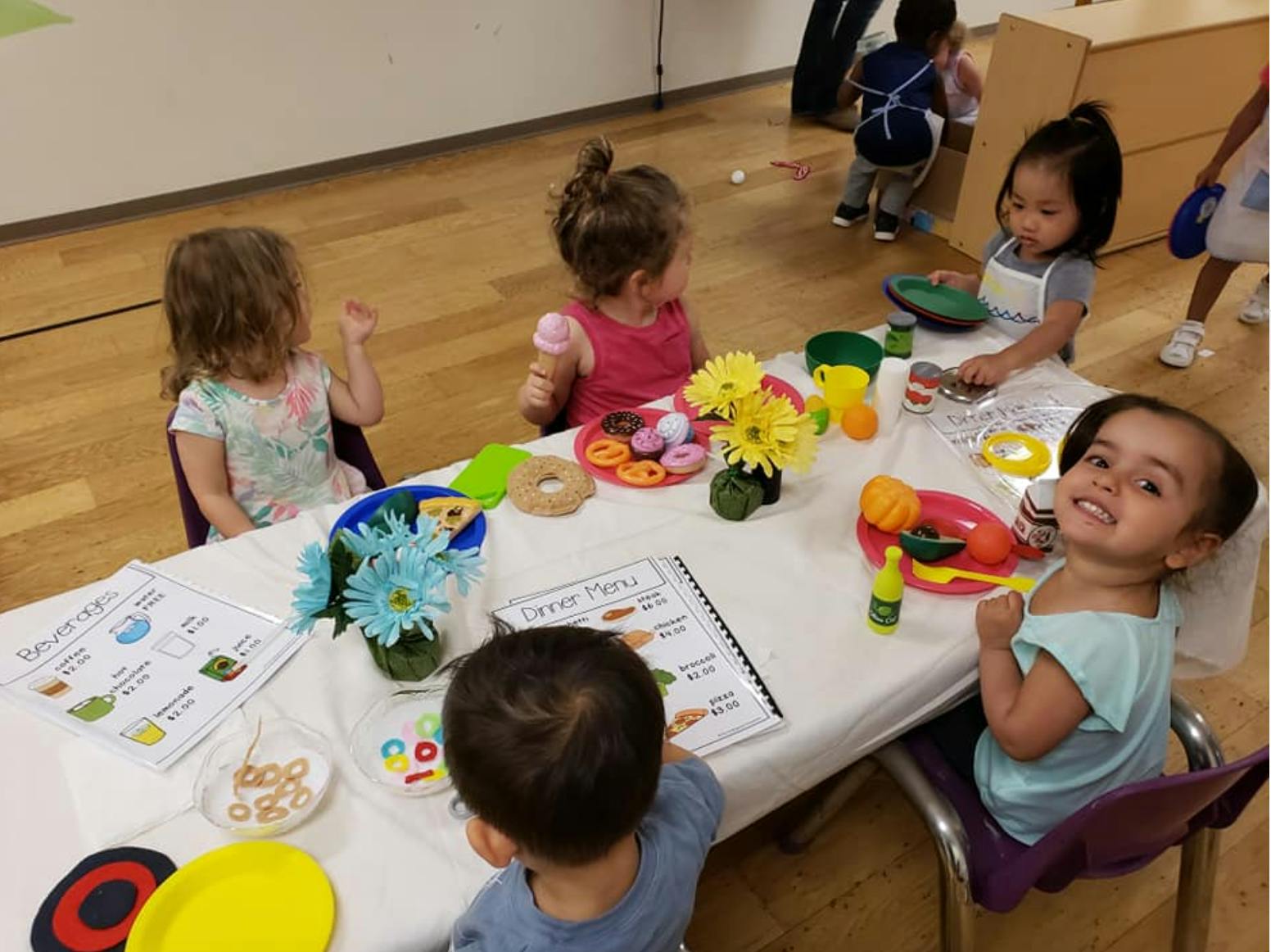Children sitting at a table with play food and flowers