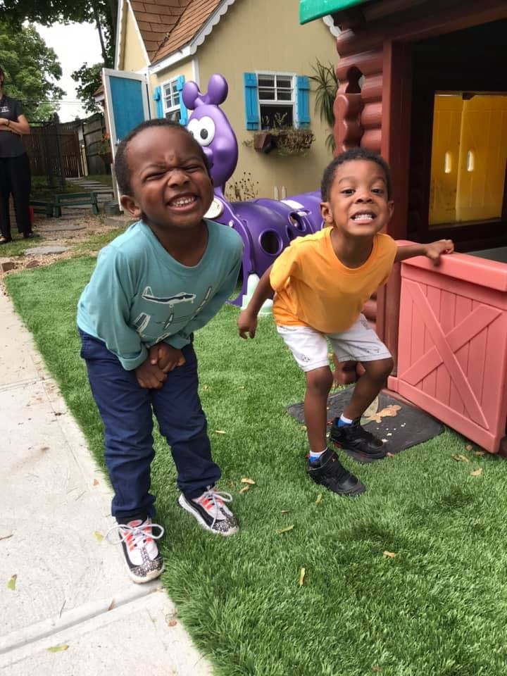 Two children standing on grass in front of a playhouse