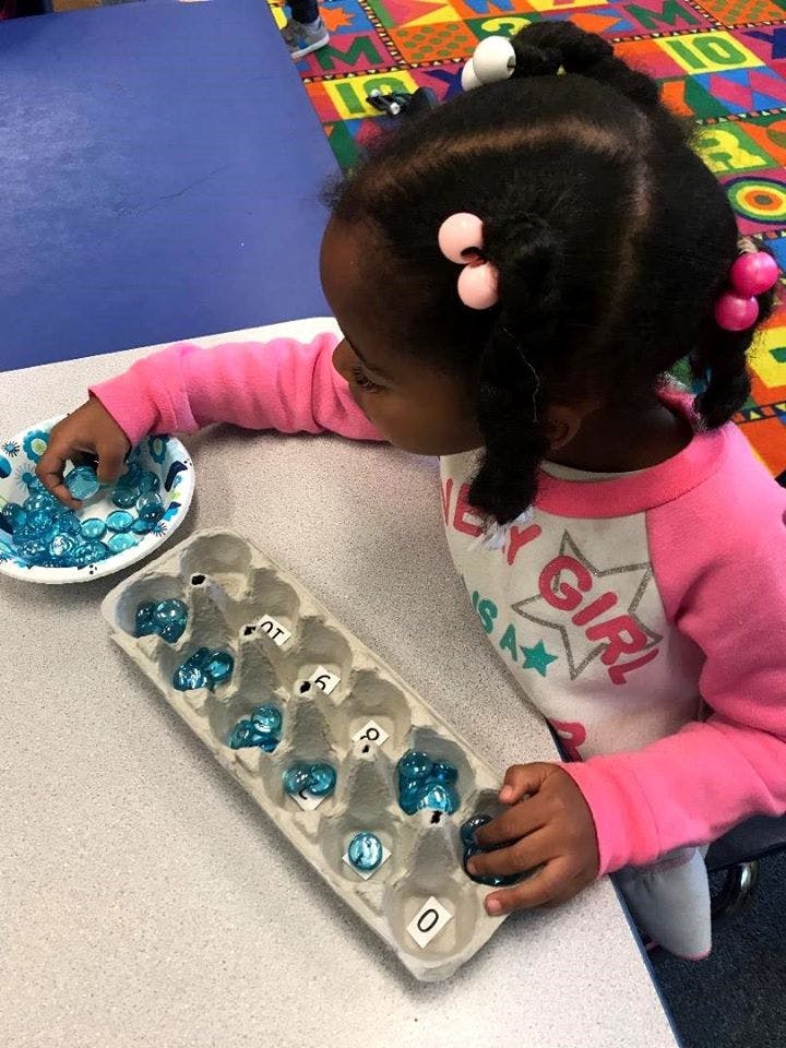 Child playing with blue objects and an egg carton with numbers