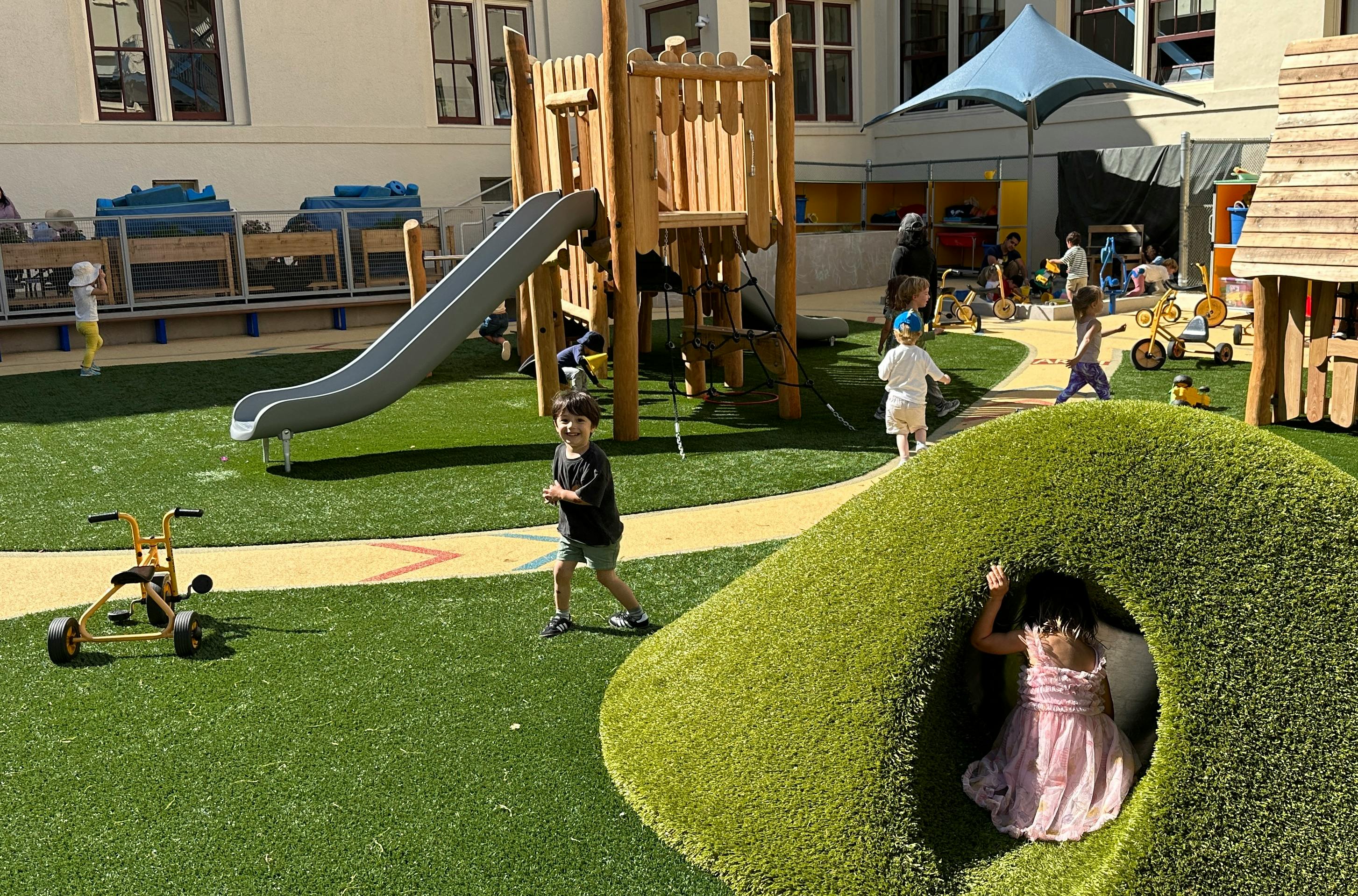Children playing on a playground with a slide and a grassy tunnel