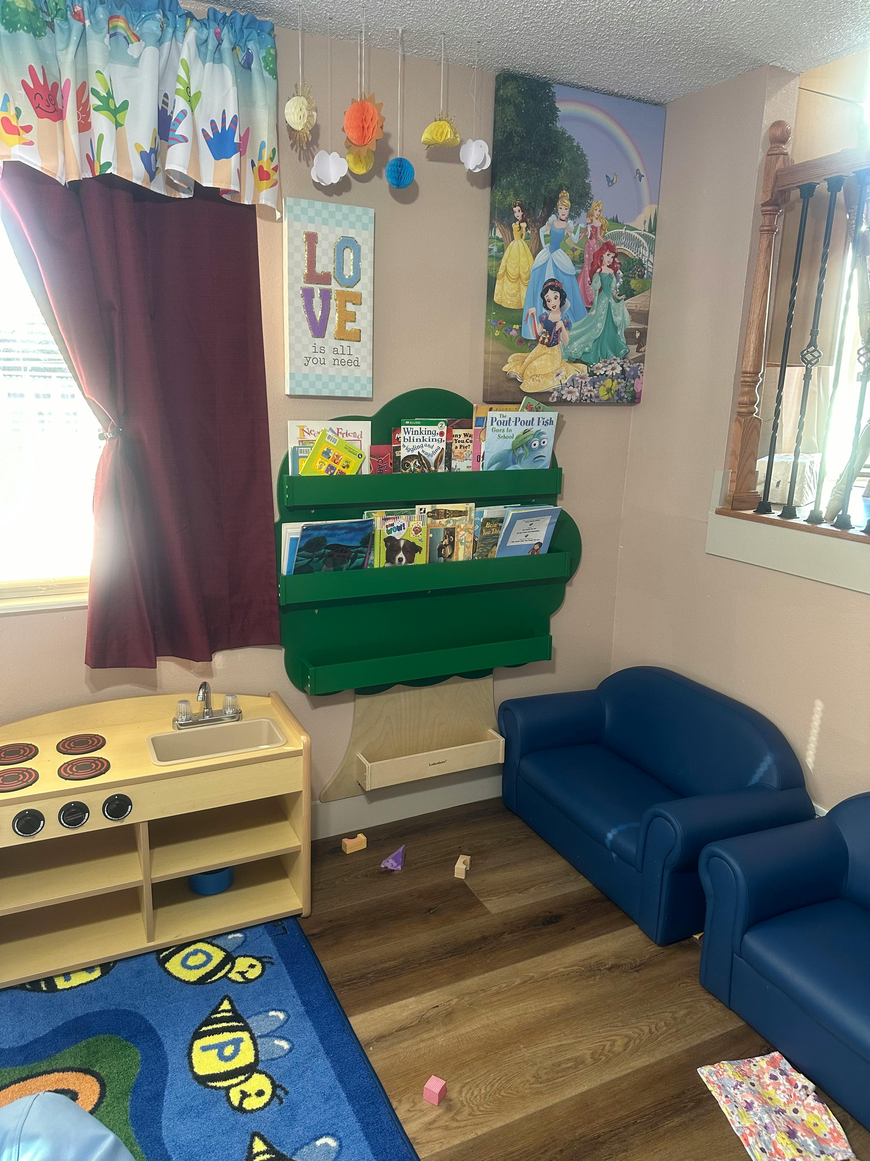 Children's play area with toy kitchen, blue couches, and a green bookshelf