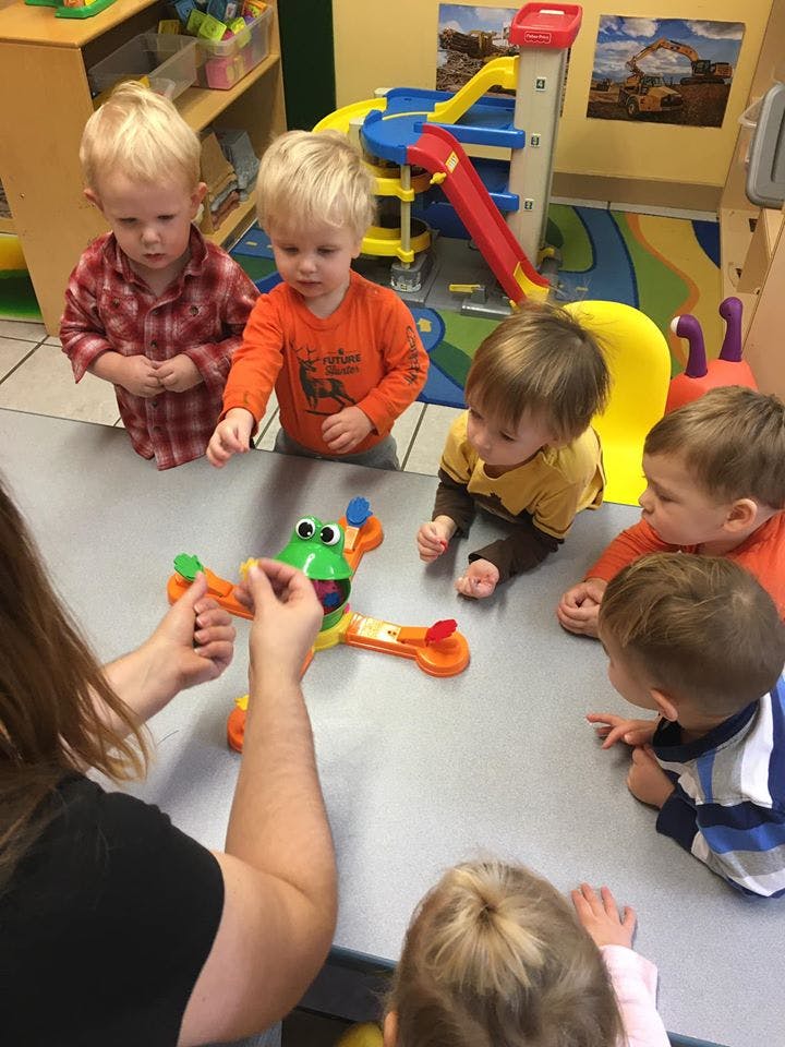Adult and multiple children gathered around a table playing with a toy frog