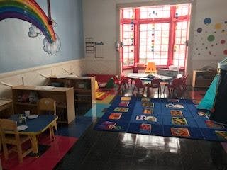 Classroom with small tables and chairs, a blue rug, and a rainbow mural
