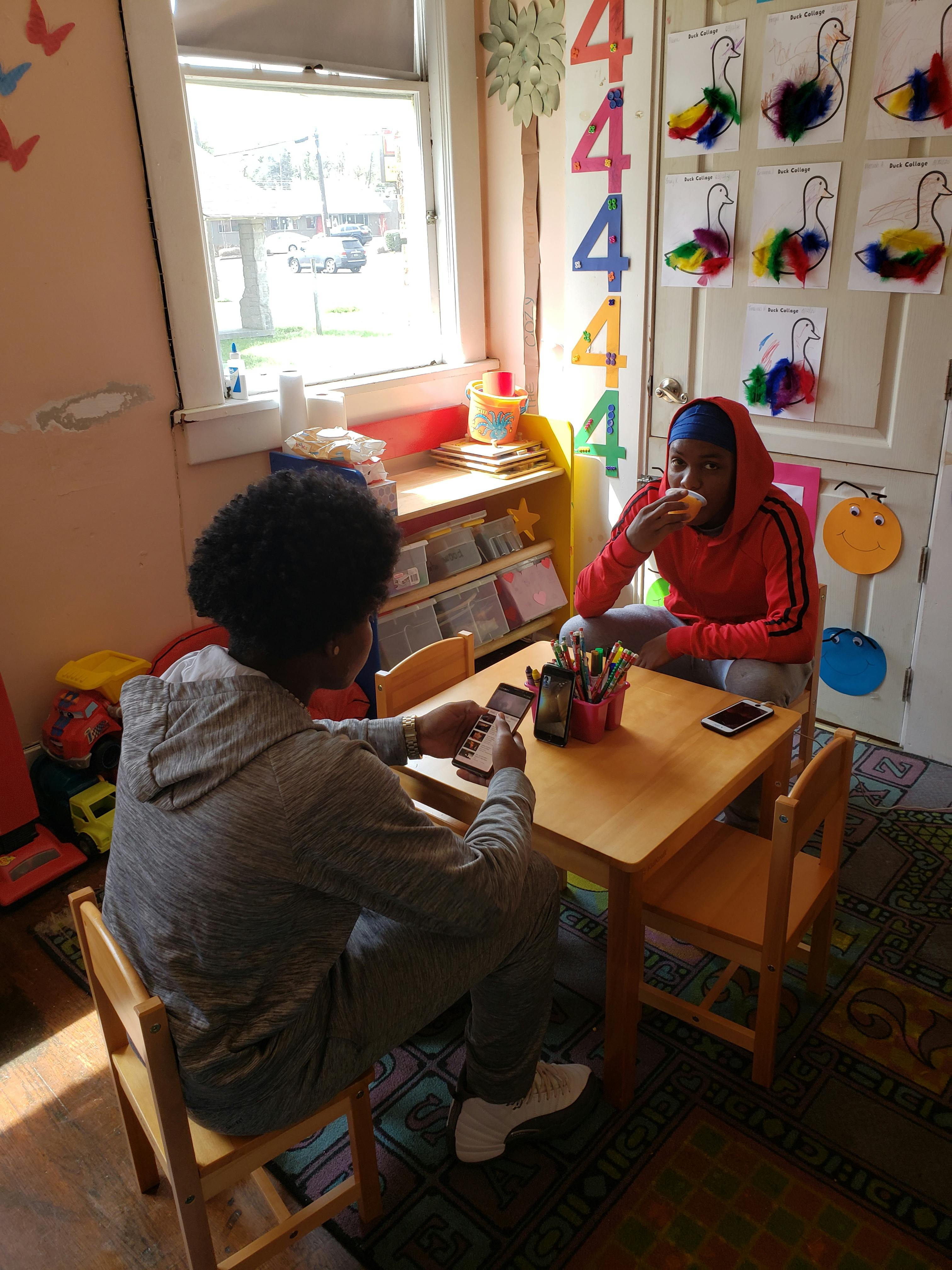 Two people sitting at a small table, one eating and one looking at a phone